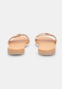 Sandales plates avec un design beige clair et blanc ; comprennent des brides minimalistes et une semelle lisse et texturée pour le confort.