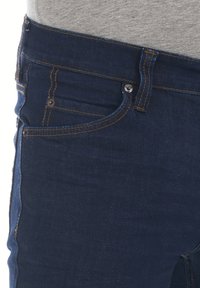 Vaqueros de mezclilla azul oscuro con un diseño clásico de cinco bolsillos, costuras de cobre y un cierre de botón en la cintura. Textura suave.