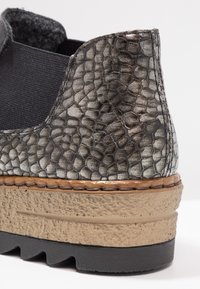 Bottine à texture métallique avec panneau latéral élastique et semelle épaisse beige avec bande de roulement noire.