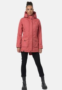 Pink waterproof parka with a hood, front buttons, and two large front pockets, worn over black pants and boots, featuring a smooth texture.
