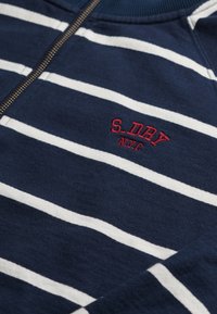 Sweatshirt bleu marine avec des rayures blanches horizontales, doté d'une fermeture éclair et d'un texte brodé rouge, "S.DRY NYC," sur le côté supérieur gauche.