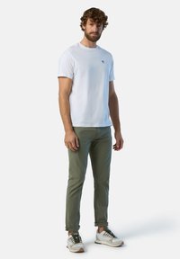 T-shirt bianco in cotone con logo blu, chinos verde oliva e sneakers bianche con dettagli grigi e marroni. Outfit semplice e casual.