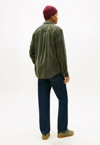 Groene corduroy shirt, relaxed fit, met achterste plooidetail. Gepaard met donkerblauwe jeans en olijfgroene schoenen. Bordeaurood geribde muts.