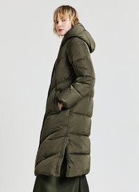 Lungo piumino verde oliva con cappuccio, design trapuntato, tasche laterali e chiusure a pressione. Materiale morbido e isolante per il calore.