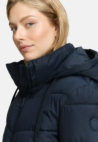 Marineblaue Steppjacke mit hohem Kragen, Reißverschluss und verstellbaren Kordeln. Glatte Textur mit glänzender Oberfläche.