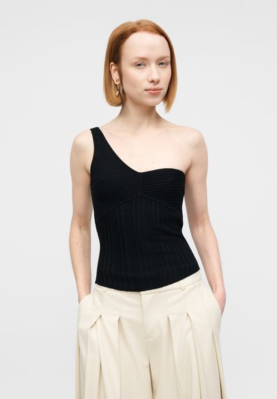 Haut en maille côtelée noire à une épaule, avec des rayures horizontales et une coupe structurée, associé à un pantalon large crème.