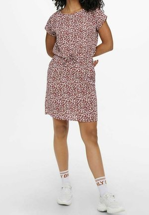 Robe rouge courte avec un motif floral blanc, coupe décontractée, col rond, manches courtes, taille élastique, portée avec des baskets blanches et des chaussettes rayées.