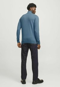 Suéter de punto azul con cuello alto, mangas largas y puños acanalados, combinado con jeans azul oscuro y calzado negro.