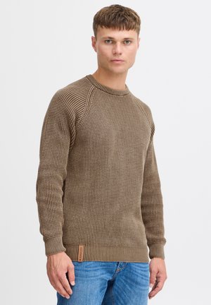 Brown textured knit sweater with a ribbed crew neckline and cuffs; features a logo tag at the hem. Paired with blue denim jeans.