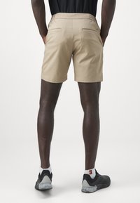 Beige shortsit, jossa on joustava vyötärö, kaksi takataskua, ommeltu helma ja kevyt kangas. Yhdistetty mustiin urheilukenkiin.