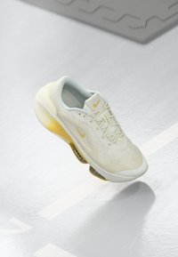 Nike trkačke tenisice u svijetlosivoj boji s žutim naglascima. Imaju teksturiranu gornjište, umanjeni potplat i zaobljeni peta za podršku.