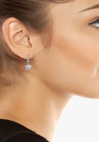 Boucles d'oreilles en argent en forme d'étoile avec une pierre précieuse transparente, présentant un design épuré et une fermeture à charnière, mises en valeur sur un fond neutre.