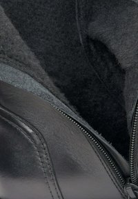 Wnętrze czarnego skórzanego buta z miękkim, ciemnym filcowym wykończeniem, z widocznym zamkiem błyskawicznym po boku i gładką skórzaną fakturą.