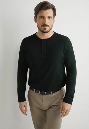 Czarna koszula henley z długim rękawem i trzema guzikami, zestawiona z beżowymi spodniami i czarnym paskiem. Gładka faktura i klasyczny krój.