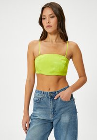 Top corto de satén verde lima con tirantes finos ajustables, escote cuadrado y una textura suave, combinado con jeans de tiro alto en azul claro.