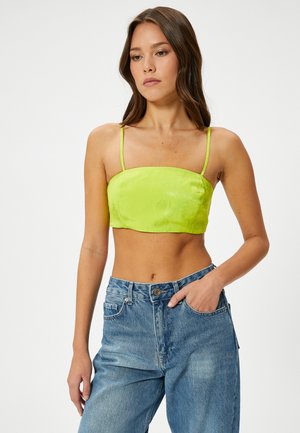 Top corto de satén verde lima con tirantes finos ajustables, escote cuadrado y una textura suave, combinado con jeans de tiro alto en azul claro.
