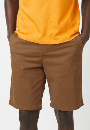 Lichte bruine shorts van een lichtgewicht stof, knielang, met zijzakken, subtiele stiksels en een gladde textuur. Gekocht in combinatie met een heldergele shirt.