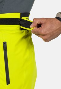 Pantaloni impermeabili giallo brillante con vita nera e tasca con zip, dotati di una regolazione sicura con strap in Velcro. Tessuto strutturato.