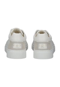 Zapatillas blancas con una parte delantera de cuero suave y trasera de ante, que cuentan con una suela de goma texturizada y una etiqueta de logo dorada en el talón.