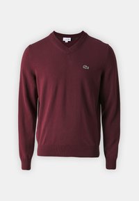 Pull en laine bordeaux à col en V, manches longues, poignets et ourlet côtelés, avec un petit logo crocodile vert brodé sur la poitrine gauche.