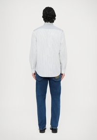 Biało-niebieska koszula w paski z zapiętym kołnierzykiem na guziki, zestawiona z niebieskimi dżinsami ozdobionymi żółtą haftowaną dekoracją na tylnej kieszeni. Casualowy krój.