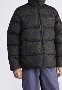 Giacca imbottita di colore verde scuro con motivo paisley, dotata di colletto alto e chiusura con zip a tutta lunghezza. Tessuto testurizzato con design trapuntato.