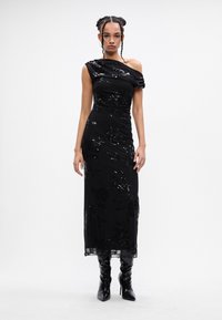 Melna, vienas pleca kleita ar ziedu izšuvumiem un paildzojiem. Šaura fit, grīdas garuma dizains apvienots ar spīdīgām, augstiem papēžiem.