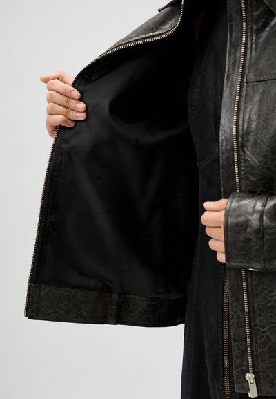 Schwarze Lederjacke mit silbernen Reißverschlüssen, ausgestattet mit einem glatten Innenfutter und einem strukturierten unteren Saum. Details umfassen ein Logo-Druck im Futter.
