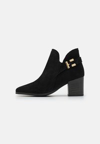 Schwarze Wildleder-Ankle-Boots mit spitzer Zehenform, ausgeschnittenen Seiten und einem goldenen Schnallenakzent. Verfügt über einen strukturierten Absatz und eine glatte Sohle.