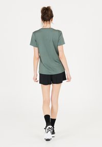 Kortärmad, olivgrön t-shirt tillsammans med svarta shorts. Slät textur, enkel design och ton-i-ton-sömmar synliga från baksidan.