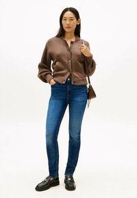 Brown ribbed cardigan with buttons, paired with blue denim jeans. Black loafers complete the outfit. Simple, casual design.