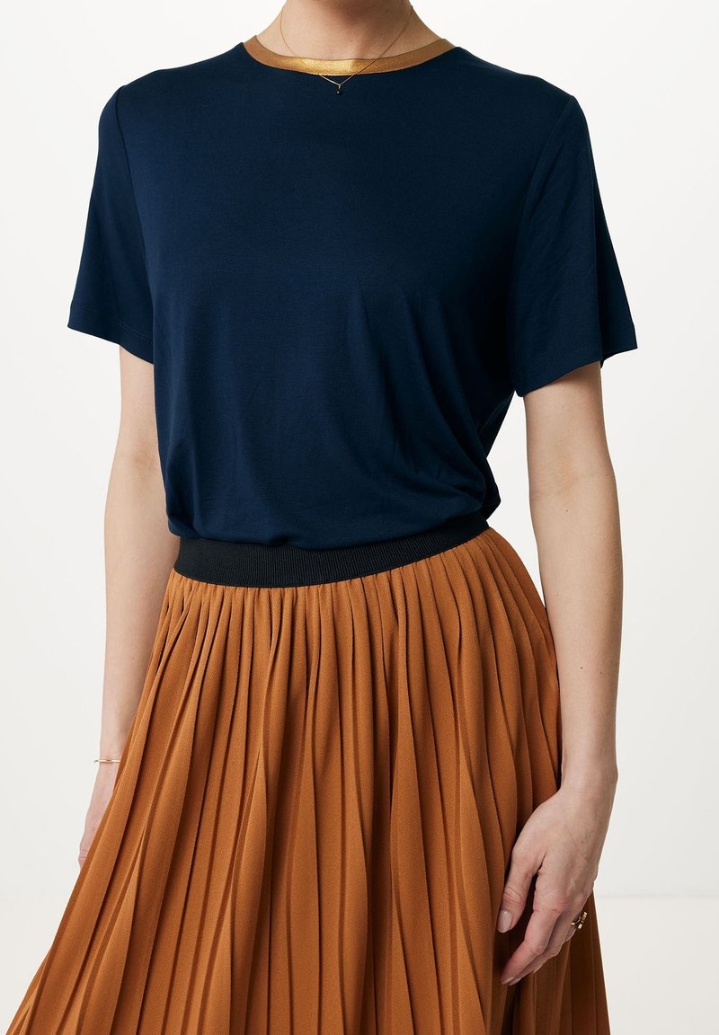 T-shirt bleu marine à manches courtes avec un col bordé d'or, associé à une jupe plissée orange dotée d'une ceinture élastique noire.