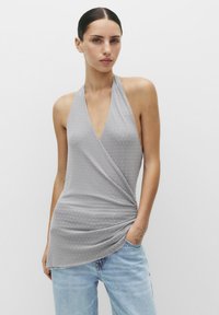 Top gri cu bretele în formă de halter, cu decolteu ad�ânc în V, prezentând un design înfășurat și un model cu puncte mici. Textură moale cu o cădere fluidă. Purtați cu blugi din denim.