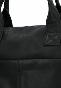 Zwarte leren tote bag met een zachte textuur, ritssluiting en versterkte handvatten met kruissteekaccenten. Merkwaarde is op de voorkant gedrukt.