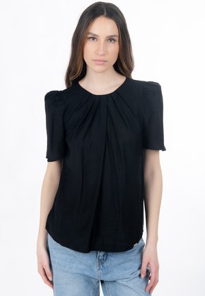 Blouse noire à manches courtes avec un design plissé, col rond et texture douce. Portée avec un jean bleu clair, mettant en valeur une coupe décontractée.