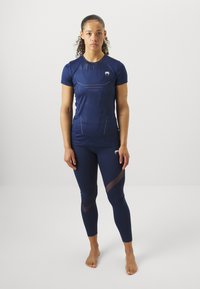 Camisa atlética azul-marinho com mangas curtas, apresenta um design texturizado e logótipo. Leggings combinando com detalhes translúcidos e forma ajustada.