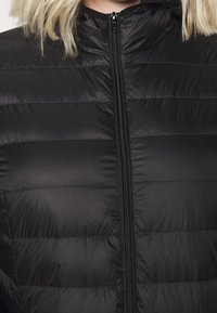 Gilet imbottito nero con pannelli trapuntati verticali, chiusura frontale con cerniera e collo alto. Tessuto liscio e lucido.