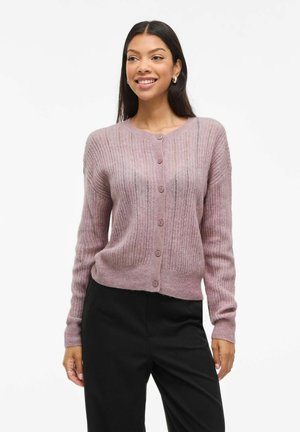 Helles rosa Cardigan aus strukturiertem Stoff mit gerippten Kanten und Knopfverschluss. Lange Ärmel mit lockerer Passform, kombiniert mit schwarzen Hosen.