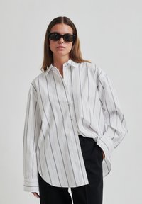 White striped long-sleeve shirt with a button-down collar. The fabric is smooth, featuring narrow grey stripes and a relaxed fit.