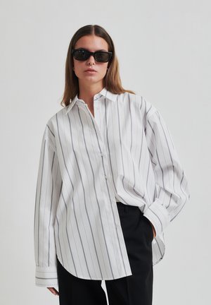 Camicia a maniche lunghe bianca a righe con colletto a button-down. Il tessuto è liscio, con sottili righe grigie e una vestibilità comoda.