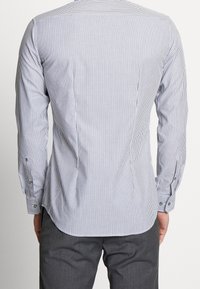 White and navy striped button-up shirt with long sleeves, a curved hem, and buttoned cuffs. Features a smooth cotton fabric texture.