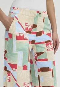Pantalons large à motifs en beige, dotés de formes abstraites en vert, rouge, bleu et marron. Comprend des poches latérales et une texture lisse.