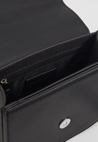 Borsa a mano in pelle nera con una texture liscia, un compartimento interno con zip e una chiusura a pressione magnetica argentata.