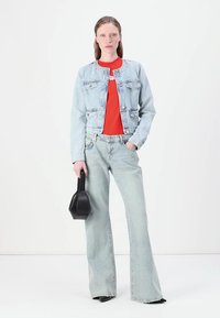 Ανοιχτό μπλε τζάκετ από τζιν με τσέπες, φορεμένο πάνω από ένα κόκκινο μπλουζάκι. Φαρδιές ανοιχτό μπλε τζιν παντελόνες και μια μαύρη τσάντα ολοκληρώνουν το σύνολο.