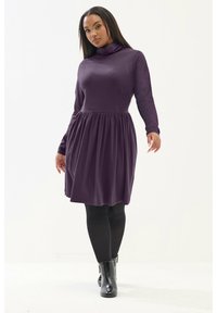 Robe longue violette à manches longues avec un col haut, taille cintrée et jupe fluide. Assortie avec des leggings noirs et des bottes à chevilles.