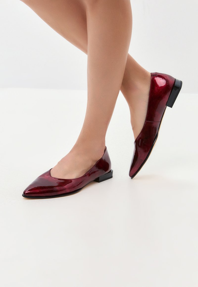 Ballerines en cuir verni rouge avec un bout pointu et un petit talon carré. Texture lisse avec une finition brillante. Vue de c�ôté montrant le placement du pied.