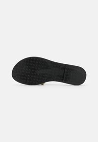Semelle d'une chaussure noire avec un motif de grip texturé, montrée à plat sur un fond gris clair.