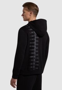 Felpa nera con cappuccio caratterizzata da un design astratto testurizzato sulla schiena. Realizzata in tessuto morbido, con tasca a marsupio e cappuccio regolabile.