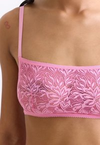 Roze kant bralette met bloemenpatronen, verstelbare schouderbandjes en golvende randen. Lichtgewicht, semi-doorzichtige stof die een zachte textuur biedt.