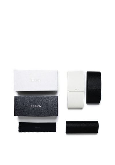 Deux étuis à lunettes Prada en blanc et noir, deux boîtes Prada assorties et un chiffon de nettoyage noir Prada sur fond blanc.